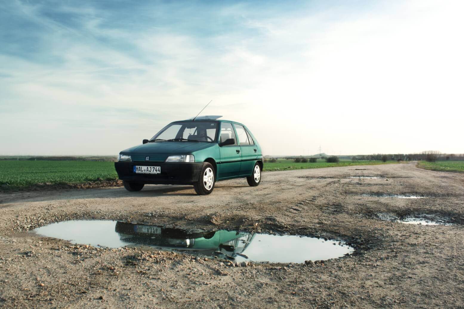 Peugeot 106 auf einem Feldweg mit Spiegelung im Wasser.